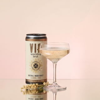 VIA sparkling brut can and glass of champagne on a light pink background