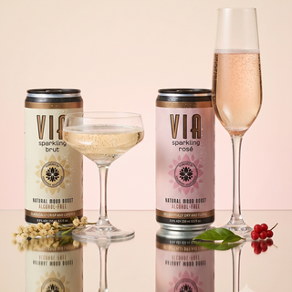 Two cans of VIA sparkling rose with two glasses filled with the drink on a beige background